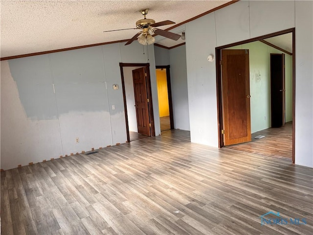 unfurnished room featuring ornamental molding, wood finished floors, a textured ceiling, a ceiling fan, and vaulted ceiling