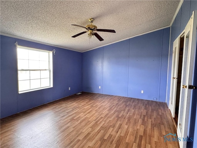 empty room featuring a textured ceiling, a ceiling fan, wood finished floors, and a decorative wall