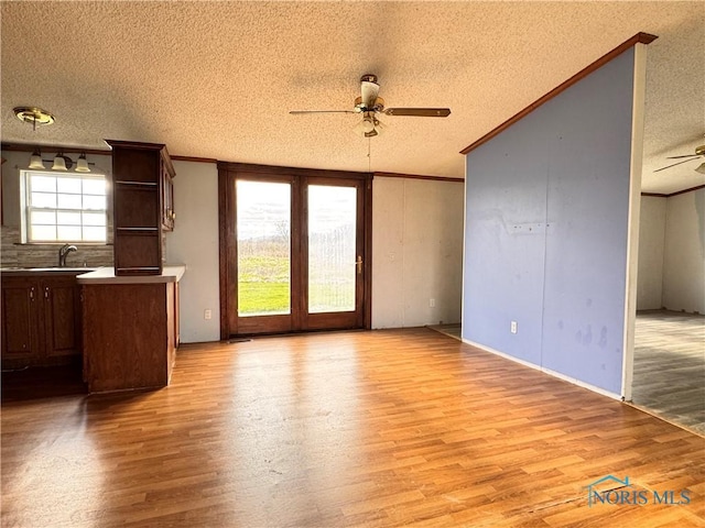 unfurnished living room with ornamental molding, ceiling fan, light wood-type flooring, a textured ceiling, and a sink