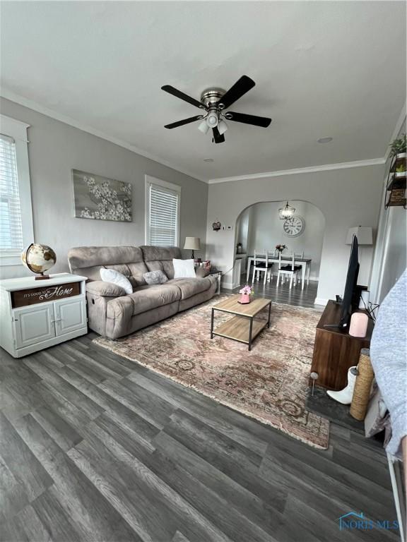living room featuring arched walkways, a ceiling fan, dark wood finished floors, and ornamental molding