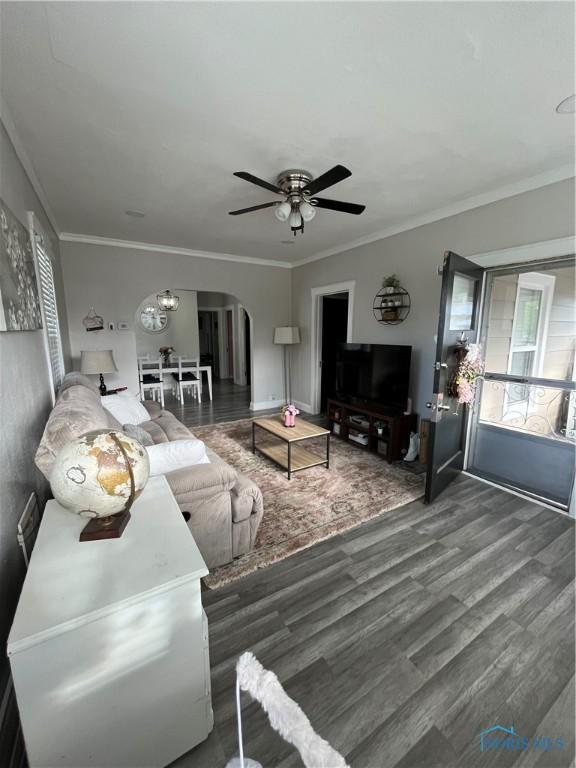 living area featuring arched walkways, ceiling fan, wood finished floors, and ornamental molding