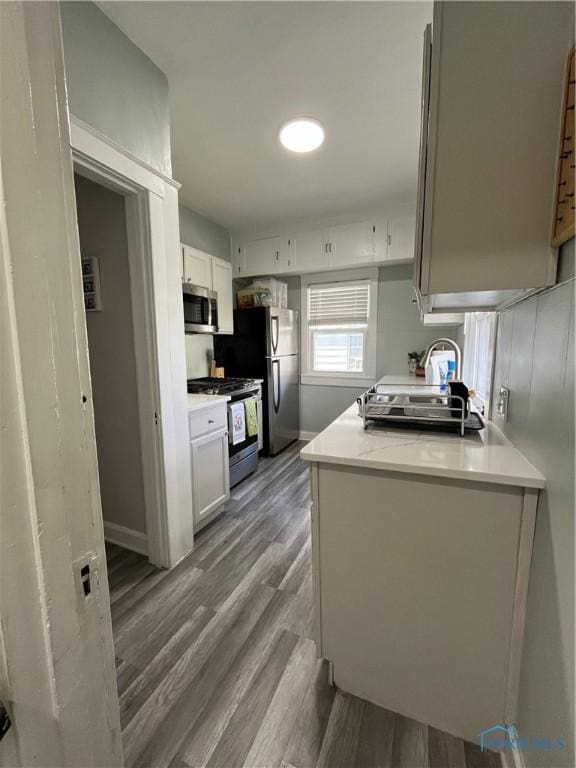 kitchen featuring white cabinets, light countertops, stainless steel appliances, baseboards, and wood finished floors