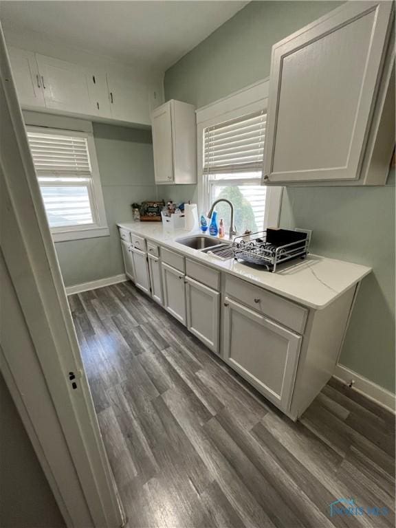 kitchen featuring light countertops, baseboards, dark wood-style floors, and a sink