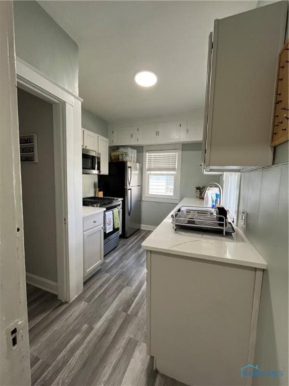 kitchen with wood finished floors, light countertops, baseboards, white cabinets, and stainless steel appliances