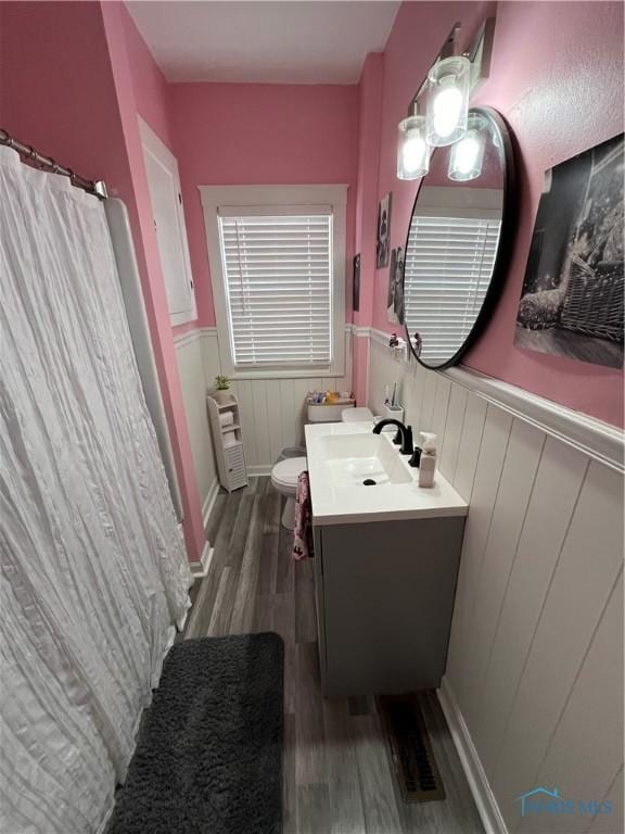 bathroom featuring vanity, toilet, a wainscoted wall, heating unit, and wood finished floors