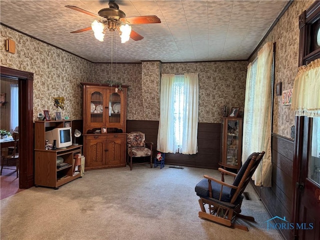 sitting room with a ceiling fan, wainscoting, wallpapered walls, and carpet flooring