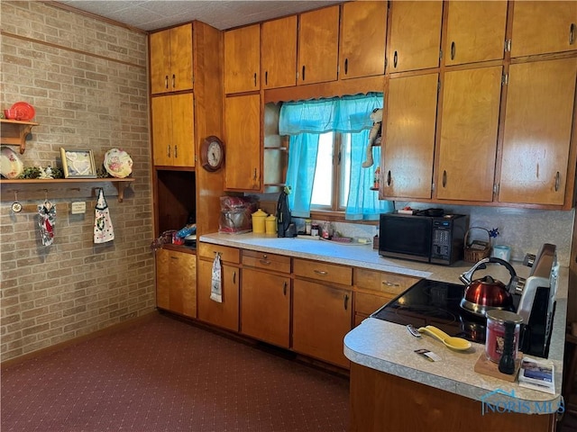 kitchen featuring brown cabinetry, light countertops, brick wall, and black microwave