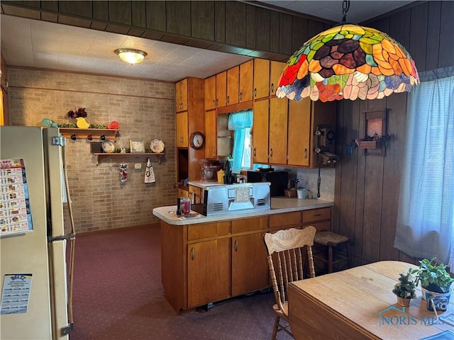 kitchen with brown cabinetry, brick wall, light countertops, freestanding refrigerator, and dark colored carpet