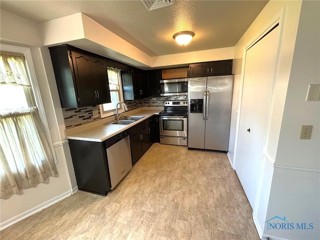 kitchen with decorative backsplash, a textured ceiling, appliances with stainless steel finishes, a sink, and light countertops