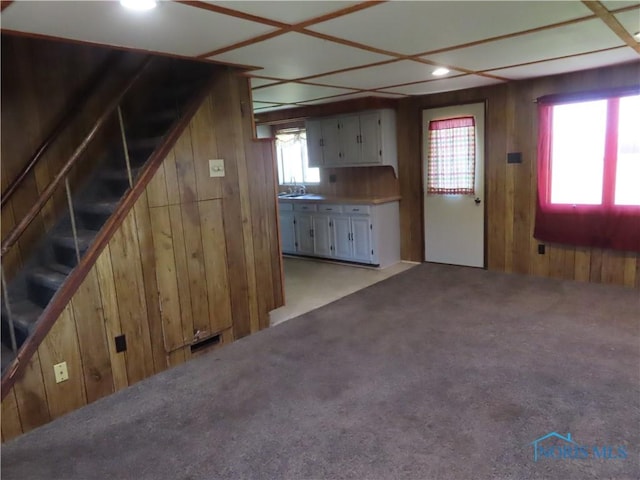 unfurnished living room with stairs, light carpet, wooden walls, recessed lighting, and a sink
