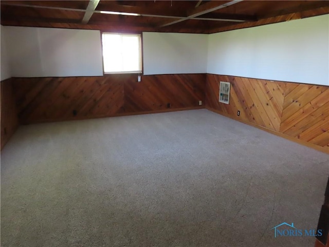 carpeted spare room with wooden walls, visible vents, and a wainscoted wall