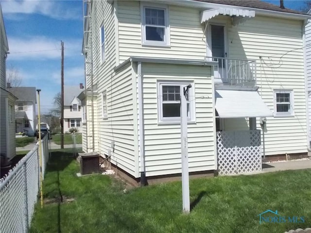 rear view of property with a lawn, central AC, fence, and a balcony