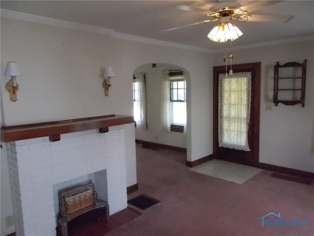 unfurnished living room with visible vents, a brick fireplace, carpet flooring, ceiling fan, and arched walkways
