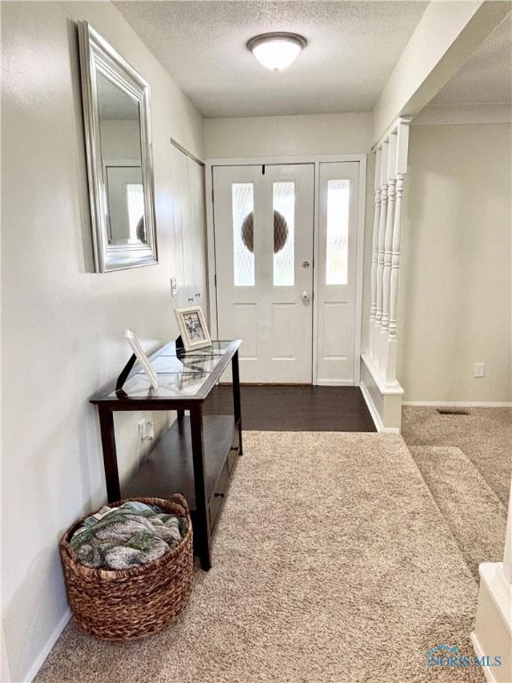 carpeted foyer entrance with baseboards and a textured ceiling
