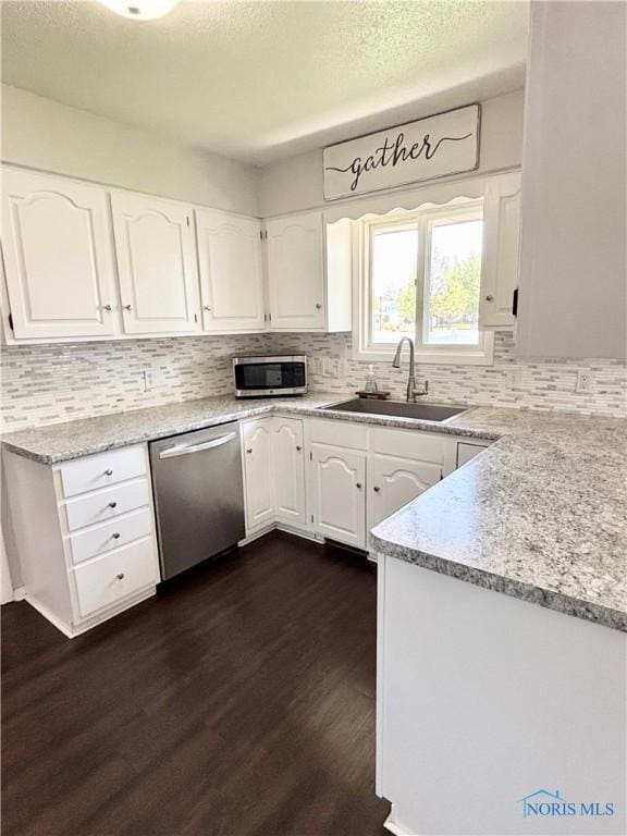 kitchen with dark wood-type flooring, a sink, appliances with stainless steel finishes, and white cabinets