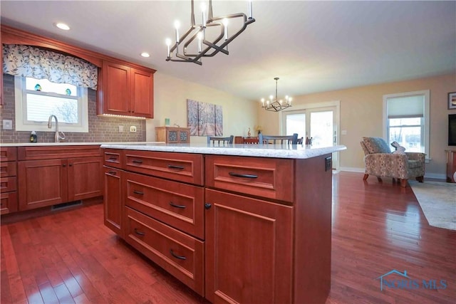 kitchen with an inviting chandelier, pendant lighting, open floor plan, a sink, and dark wood finished floors