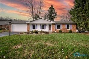 ranch-style home with a garage, a lawn, and driveway