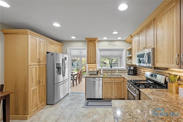 kitchen with light brown cabinetry, stainless steel appliances, light stone countertops, and a sink