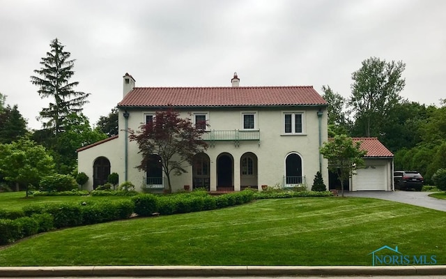 mediterranean / spanish home featuring a front lawn, a balcony, a chimney, an attached garage, and driveway