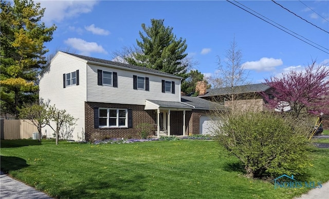 traditional home featuring brick siding, an attached garage, fence, and a front yard