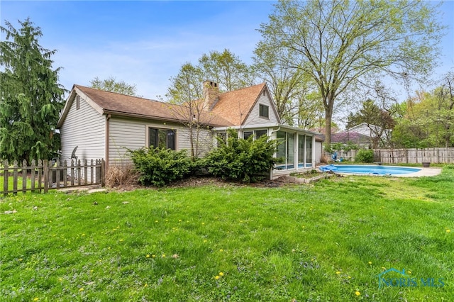 back of house with a chimney, a lawn, a sunroom, a fenced in pool, and a fenced backyard