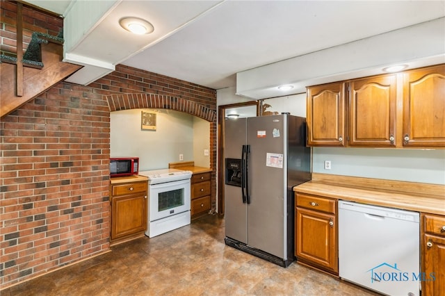 kitchen featuring tile patterned floors, brick wall, white appliances, and brown cabinets