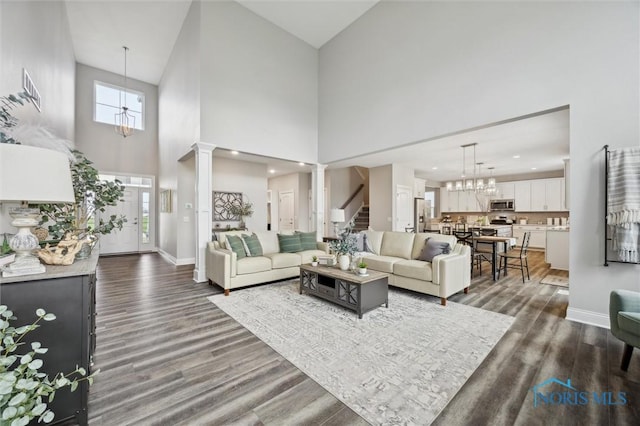 living area with stairs, dark wood-style flooring, baseboards, a high ceiling, and a notable chandelier