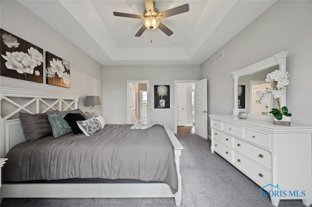 bedroom with a raised ceiling, ceiling fan, visible vents, and carpet