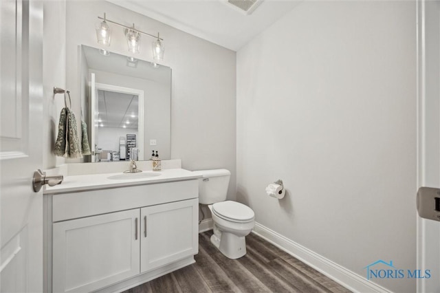 half bath with vanity, visible vents, wood finished floors, toilet, and baseboards