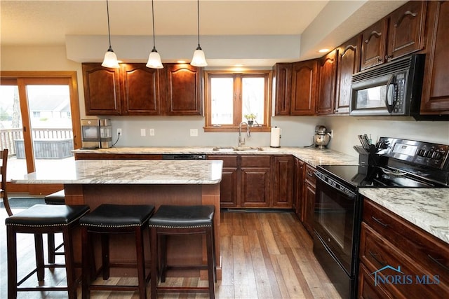 kitchen featuring a sink, a breakfast bar, black appliances, and a wealth of natural light