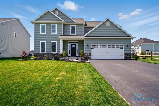 craftsman-style house with fence, a front yard, stone siding, an attached garage, and driveway