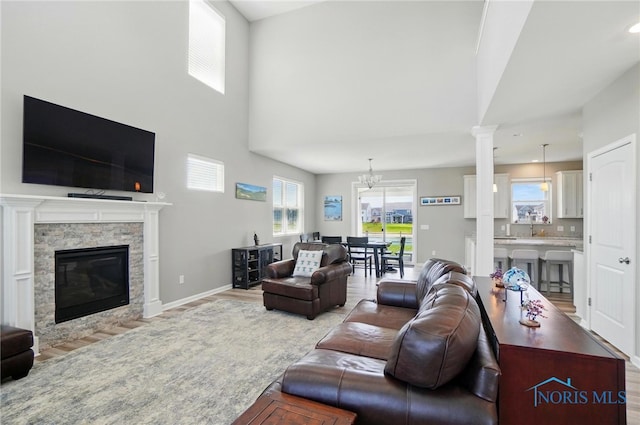 living area with baseboards, an inviting chandelier, a stone fireplace, and light wood-type flooring