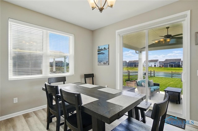 dining space featuring baseboards, light wood-style flooring, a water view, and ceiling fan with notable chandelier