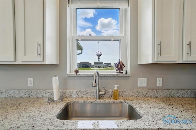 details featuring white cabinets, light stone counters, and a sink