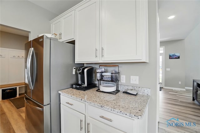 kitchen with light wood-type flooring, baseboards, light stone counters, white cabinets, and freestanding refrigerator