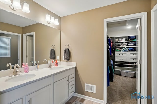 bathroom with a sink, a walk in closet, double vanity, and visible vents