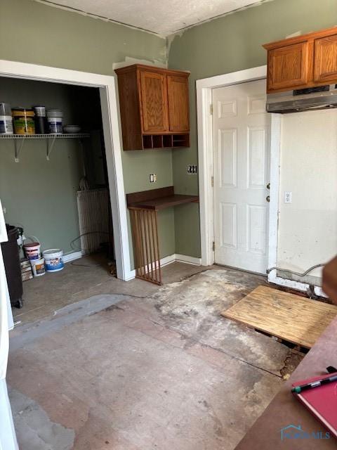 kitchen featuring concrete floors, under cabinet range hood, and brown cabinets