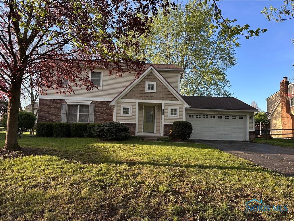 traditional-style house with driveway, a garage, brick siding, fence, and a front lawn