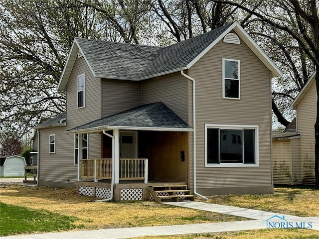 traditional-style house with a front lawn, roof with shingles, and covered porch