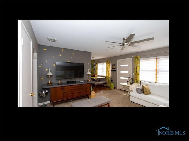 living room with light carpet, a ceiling fan, wallpapered walls, baseboards, and visible vents
