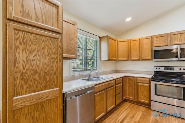 kitchen featuring appliances with stainless steel finishes, a sink, light wood-style floors, light countertops, and vaulted ceiling