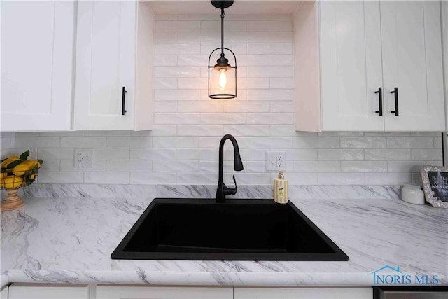 kitchen with a sink, light stone counters, backsplash, and white cabinetry