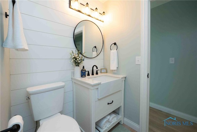 half bath with vanity, baseboards, wood finished floors, and toilet