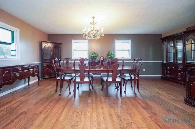 dining room with baseboards, light wood finished floors, and a notable chandelier