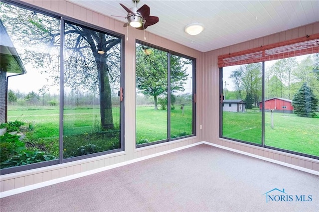 unfurnished sunroom featuring carpet flooring, ceiling fan, and wooden walls