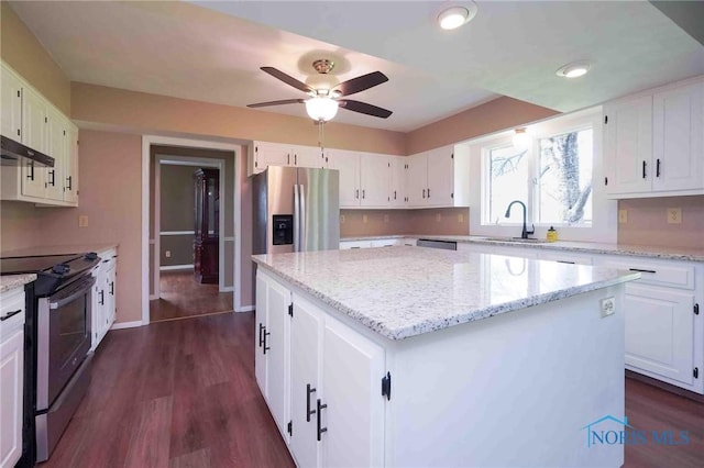 kitchen with ceiling fan, appliances with stainless steel finishes, light stone counters, a sink, and a center island