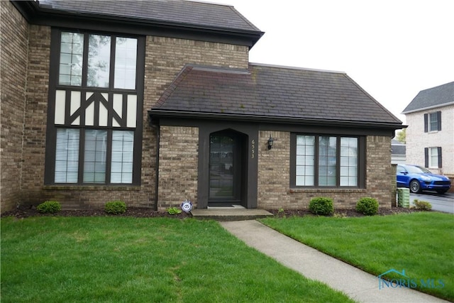 exterior space featuring brick siding, a high end roof, and a front yard