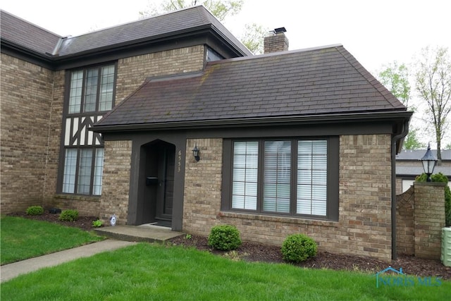 view of front of property with roof with shingles, a chimney, a front yard, and brick siding