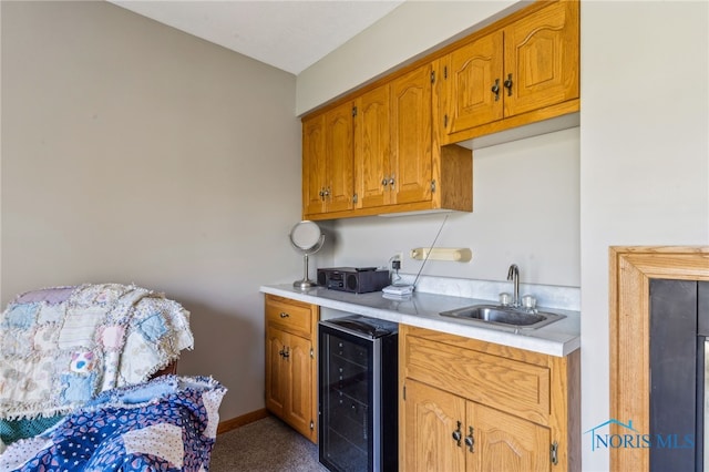 kitchen featuring brown cabinets, a sink, light countertops, beverage cooler, and carpet floors