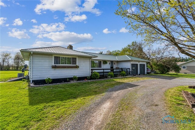view of front of property featuring an attached garage, a front yard, a chimney, driveway, and metal roof